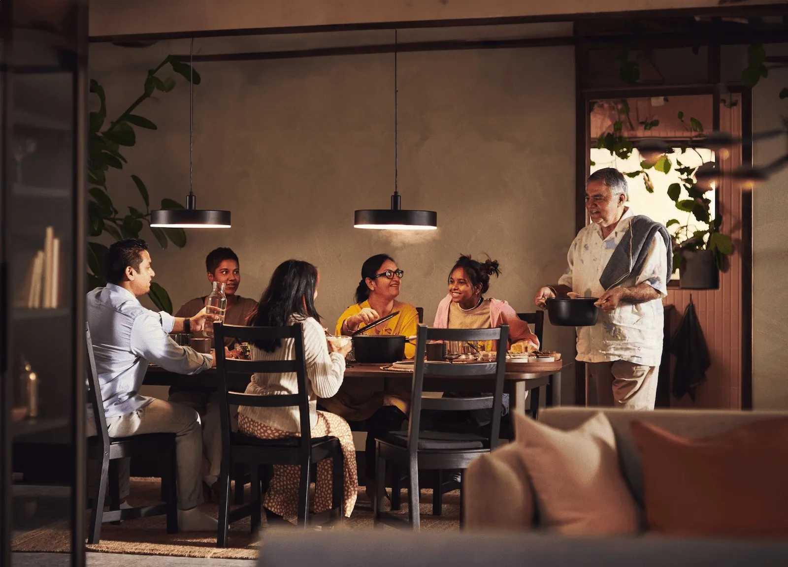 Family gathered around a dinner table in a warm, inviting home, sharing a meal and conversation, representing the comfort and connection that come with achieving homeownership and being closer to home than you think.